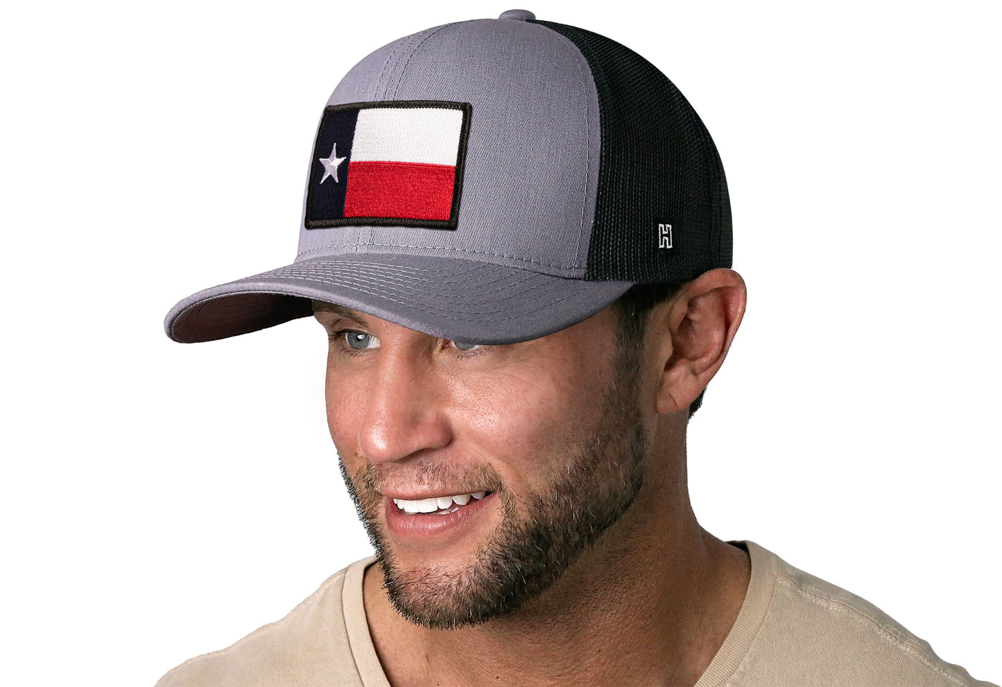 Gray-Black trucker hat worn by a male model viewed from the left side and features a Texas Gray-Black TX Embroidered Flag Patch displayed on the front panel. The hat has a classic mesh back design and a curved structured bill