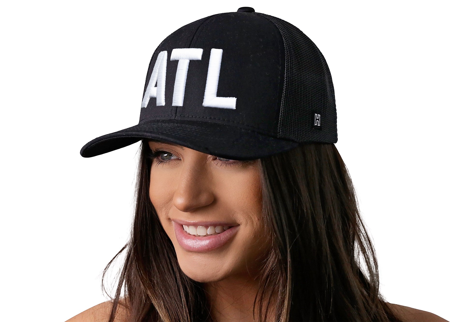 Black trucker hat worn by a female model viewed from the left side and features a ATL 3-D Puff Direct Embroidery displayed on the front panel. The hat has a classic mesh back design and a curved structured bill