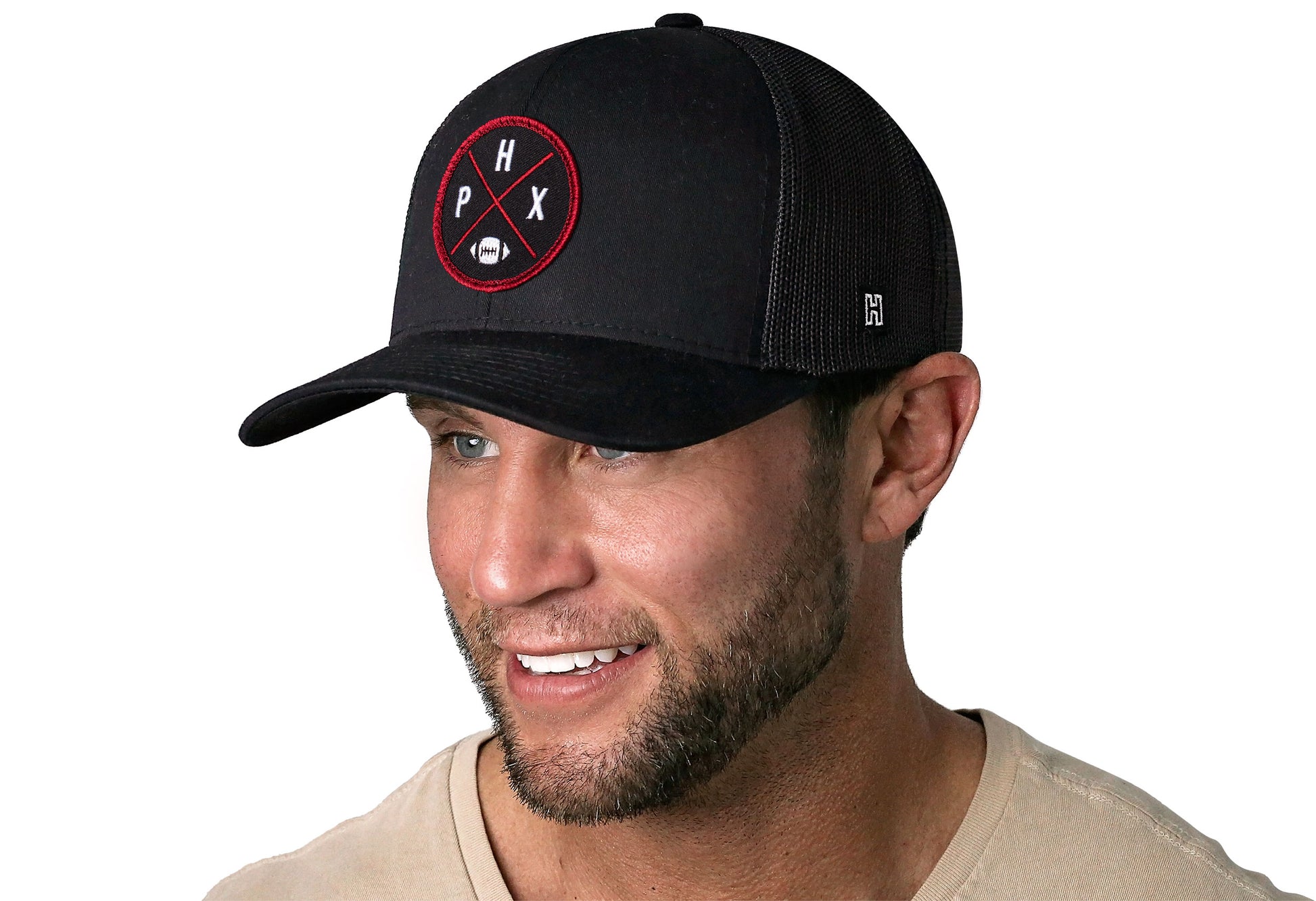 black trucker hat worn by a male model viewed from the left side and features a bold scarlet and black embroidered X patch displayed on the front panel. The hat has a classic mesh back design and a curved structured bill