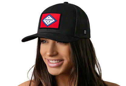 Black trucker hat worn by a female model viewed from the left side and features a Arkansas Flag Embroidered Rectangle Patch displayed on the front panel. The hat has a classic mesh back design and a curved structured bill