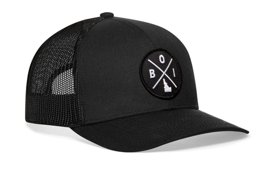 Black trucker hat viewed from the right side, showcasing a Boise BOI X Embroidered Circle Patch prominently displayed on the front