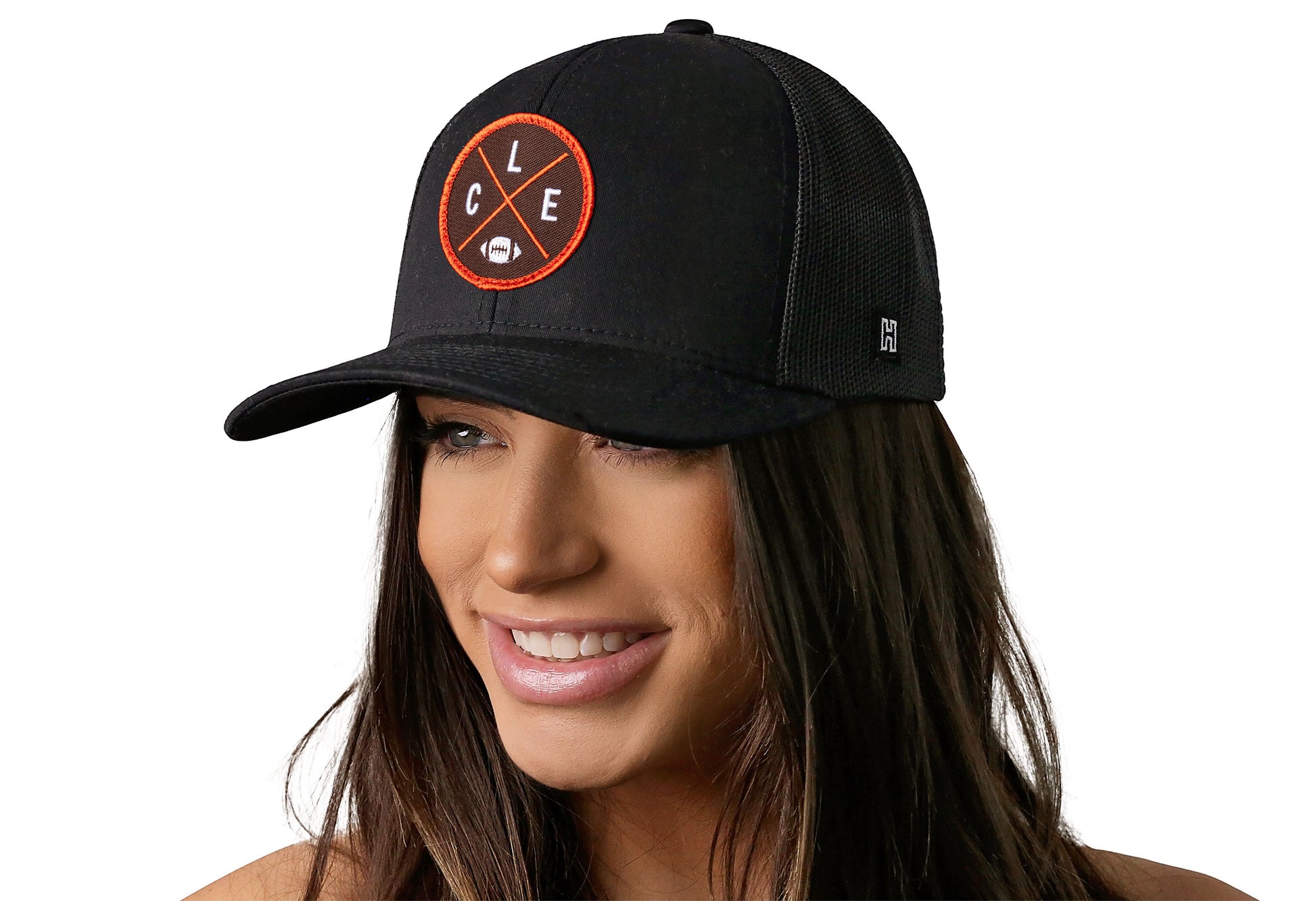 black trucker hat worn by a female model viewed from the left side and features a bold orange, and brown embroidered X patch displayed on the front panel. The hat has a classic mesh back design and a curved structured bill