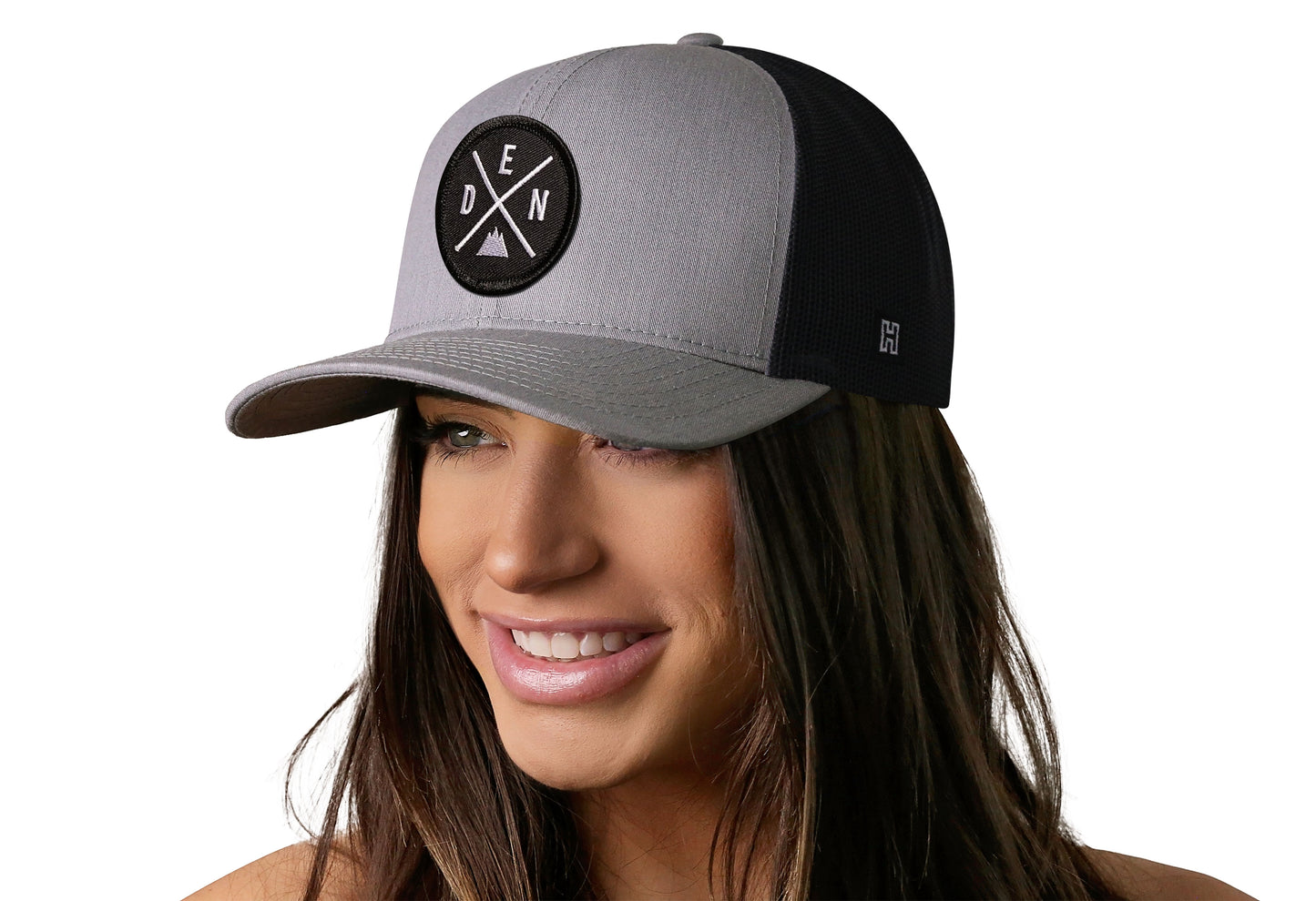 Gray-Black trucker hat worn by a female model viewed from the left side and features a Denver DEN X Embroidered Circle Patch displayed on the front panel. The hat has a classic mesh back design and a curved structured bill