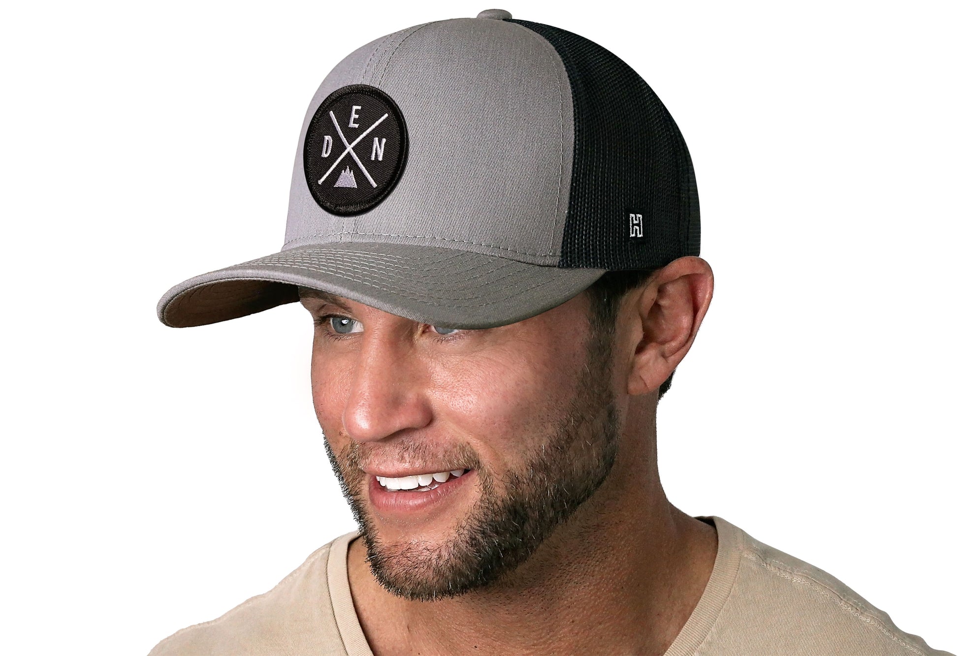 Gray-Black trucker hat worn by a male model viewed from the left side and features a Denver DEN X Embroidered Circle Patch displayed on the front panel. The hat has a classic mesh back design and a curved structured bill