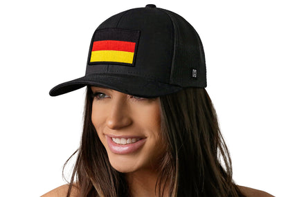 Black trucker hat worn by a female model viewed from the left side and features a German Flag Embroidered Rectangle Patch displayed on the front panel. The hat has a classic mesh back design and a curved structured bill