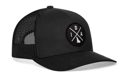 Black trucker hat viewed from the right side, showcasing a Idaho IDA X Embroidered Circle Patch prominently displayed on the front