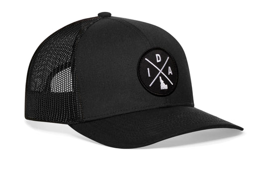 Black trucker hat viewed from the right side, showcasing a Idaho IDA X Embroidered Circle Patch prominently displayed on the front