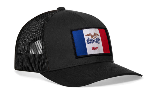 Black trucker hat viewed from the right side, showcasing a Iowa Woven Rectangle Patch prominently displayed on the front