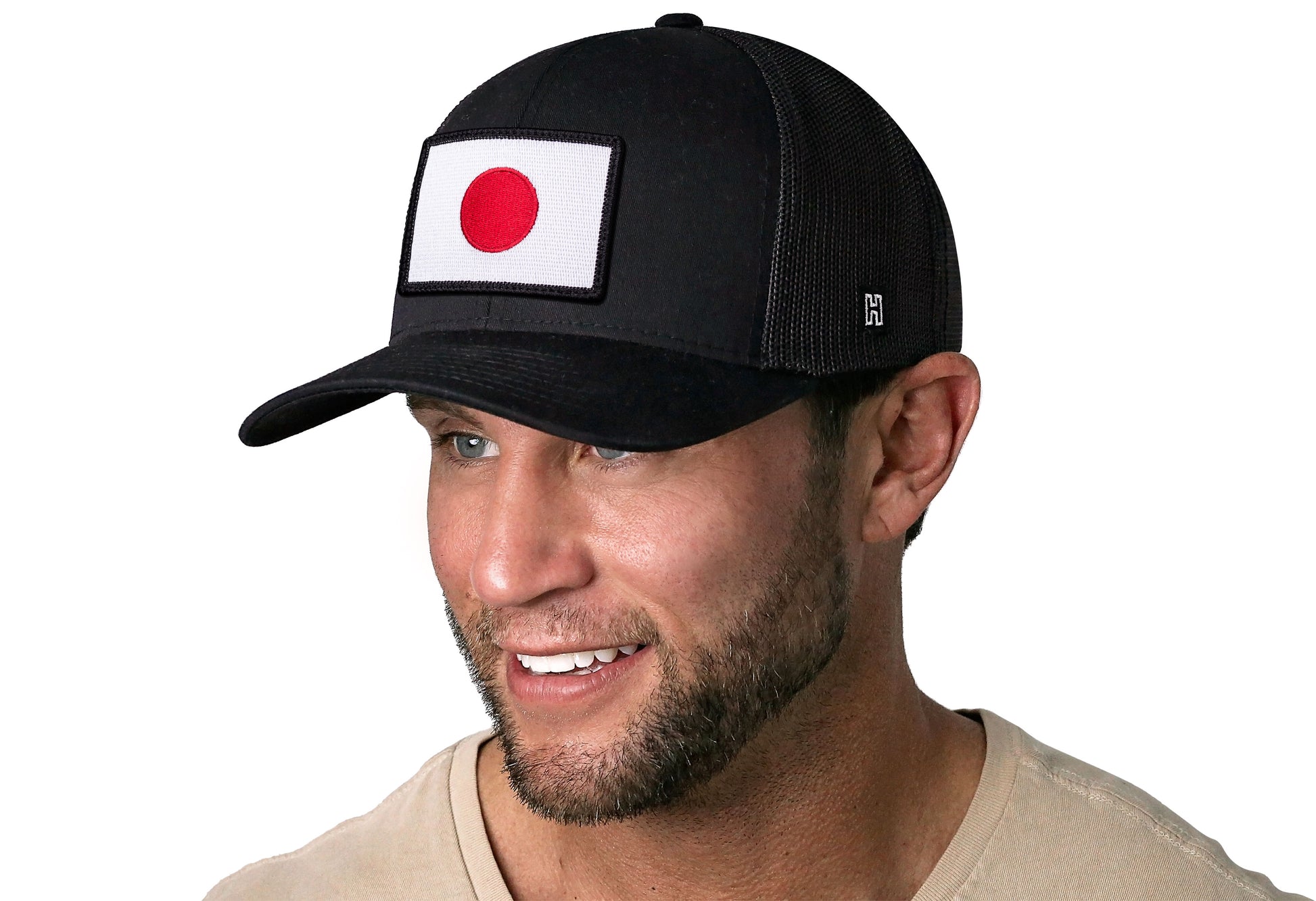 Black trucker hat worn by a male model viewed from the left side and features a Japanese Flag Embroidered Rectangle Patch displayed on the front panel. The hat has a classic mesh back design and a curved structured bill