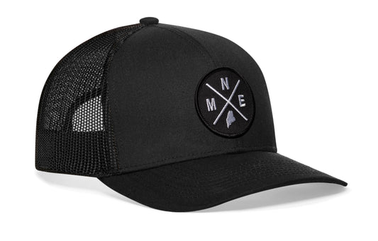 Black trucker hat viewed from the right side, showcasing a Maine MNE X Embroidered Circle Patch prominently displayed on the front