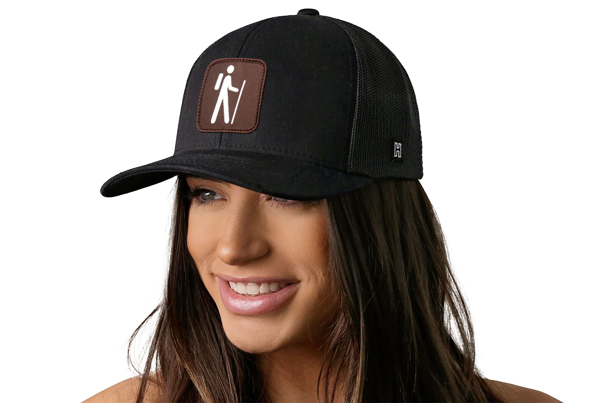 Black trucker hat worn by a female model viewed from the left side and features a NP Trailhead Pictographic Symbols Embroidered Patch displayed on the front panel. The hat has a classic mesh back design and a curved structured bill