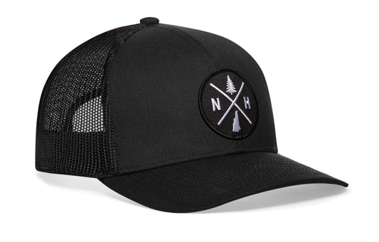 Black trucker hat viewed from the right side, showcasing a New Hampshire NH X Embroidered Circle Patch prominently displayed on the front