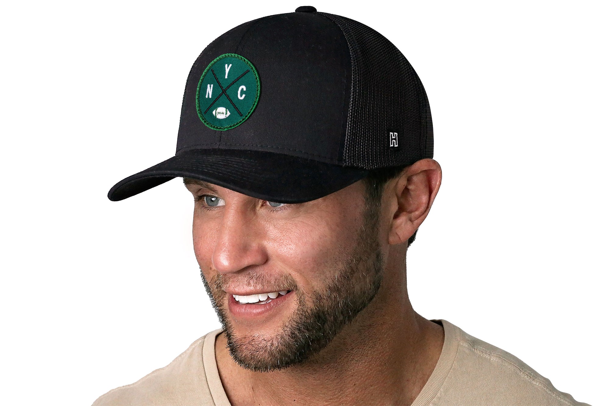 black trucker hat worn by a male model viewed from the left side and features a bold green and white embroidered X patch displayed on the front panel. The hat has a classic mesh back design and a curved structured bill
