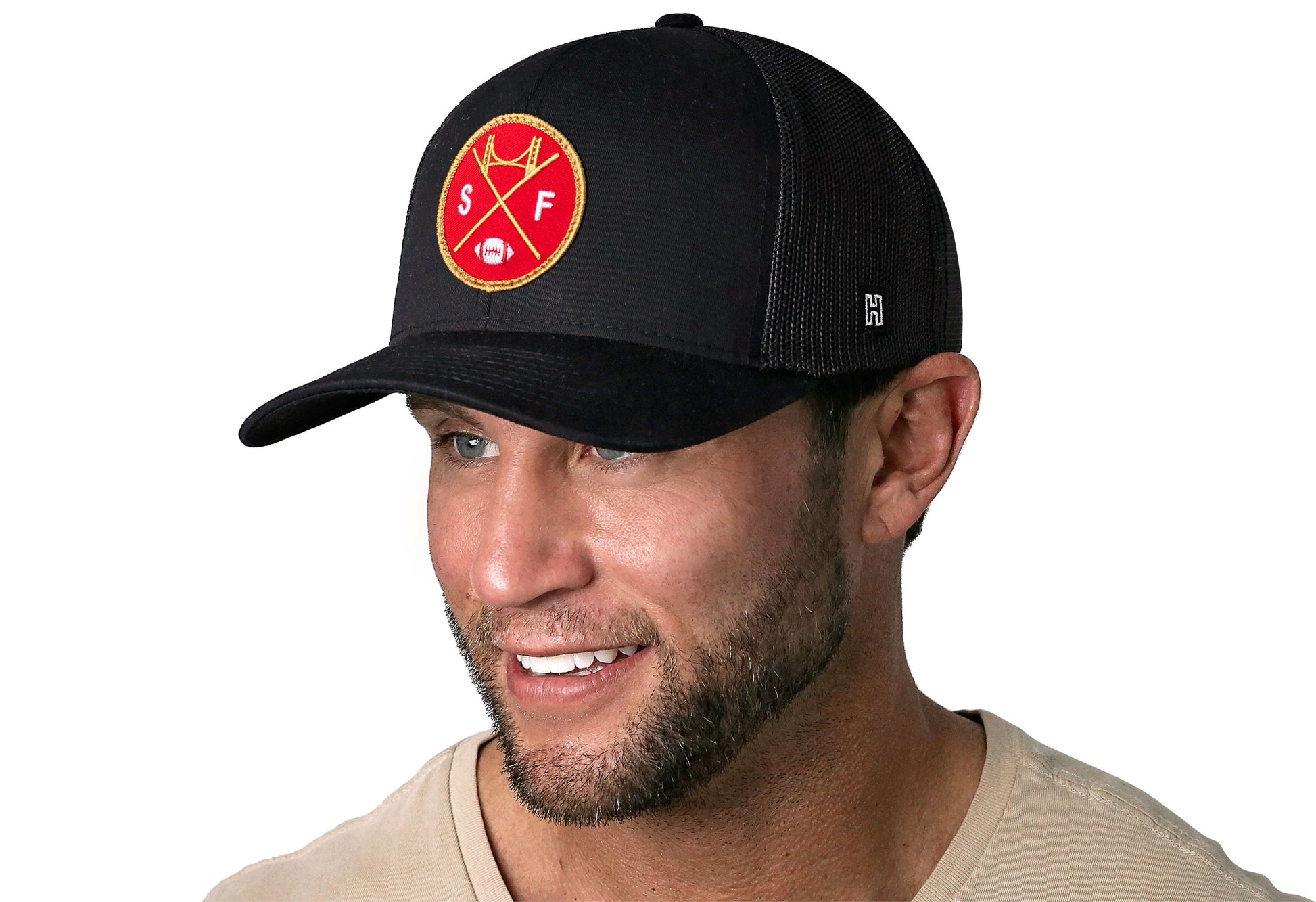 black trucker hat worn by a male model viewed from the left side and features a bold red and gold embroidered X patch displayed on the front panel. The hat has a classic mesh back design and a curved structured bill