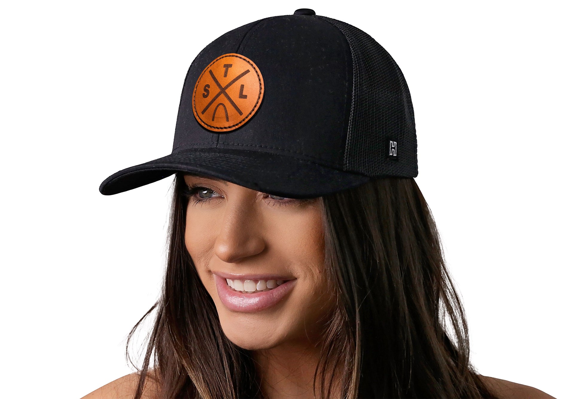 Black trucker hat worn by a female model viewed from the left side and features a St Louis STL X Leather Circle Patch displayed on the front panel. The hat has a classic mesh back design and a curved structured bill