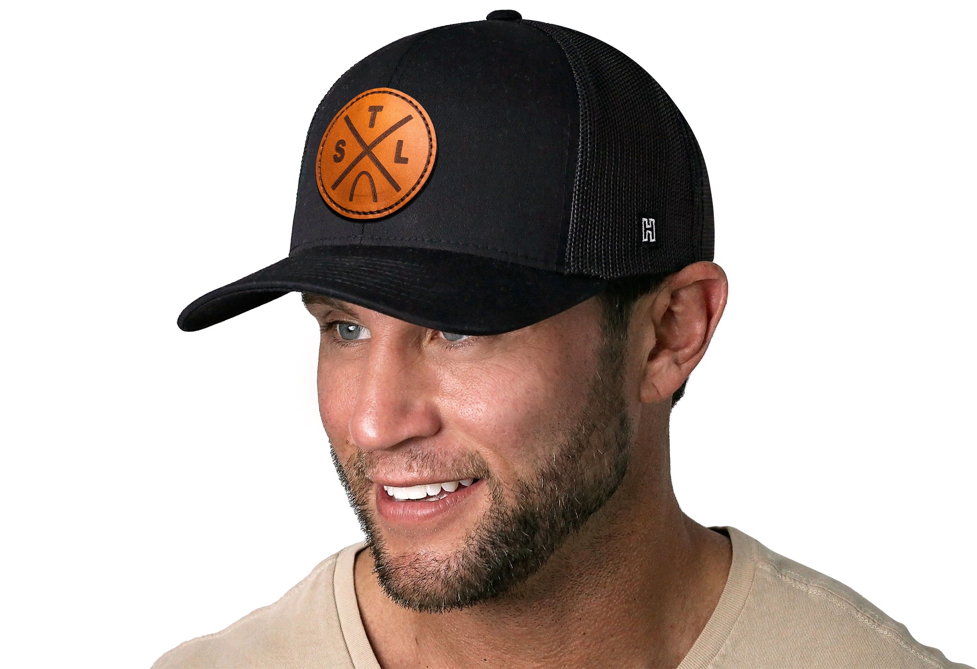 Black trucker hat worn by a male model viewed from the left side and features a St Louis STL X Leather Circle Patch displayed on the front panel. The hat has a classic mesh back design and a curved structured bill