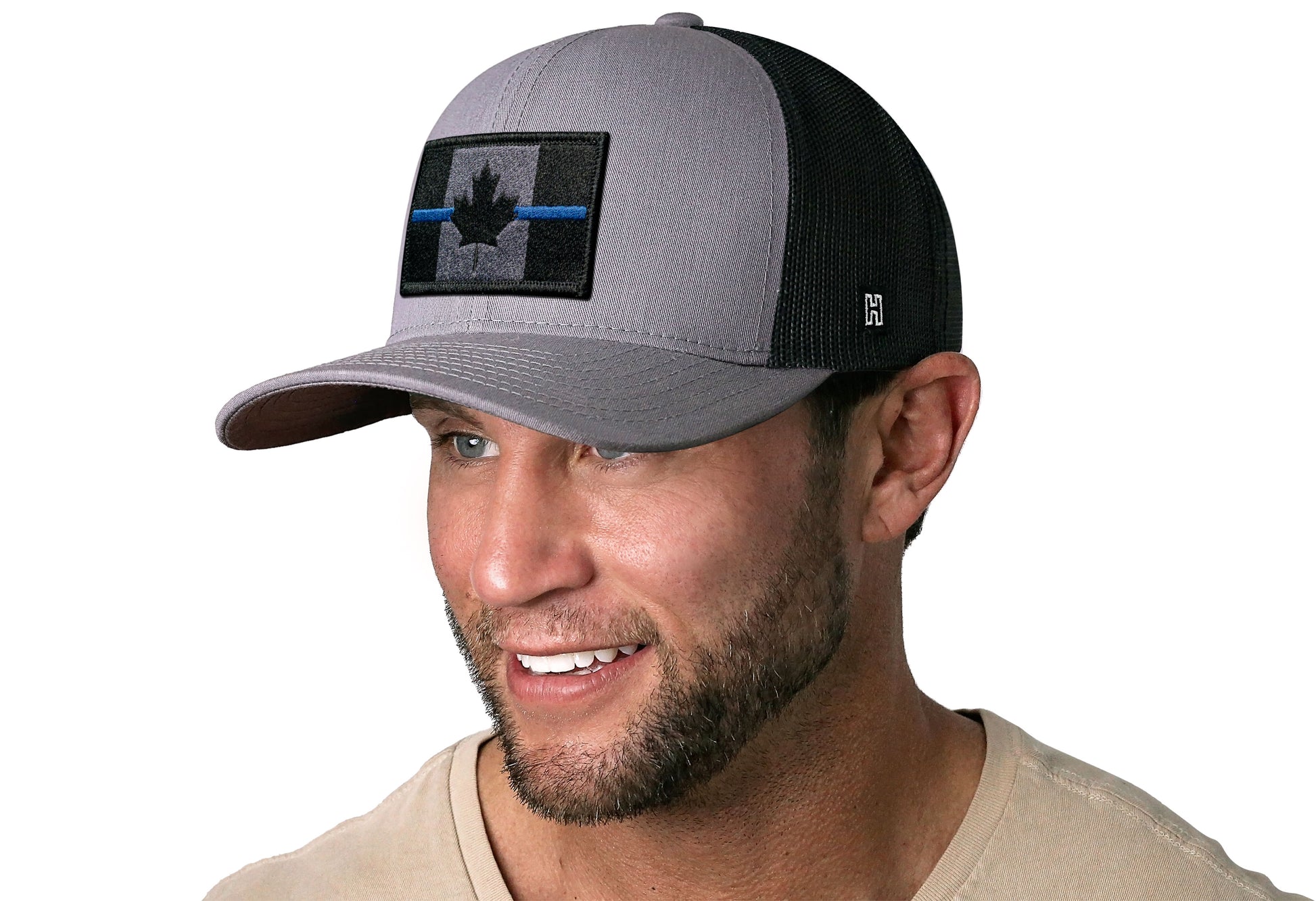 Gray-Black trucker hat worn by a male model viewed from the left side and features a Thin Blue Canadian Flag Embroidered Rectangle Patch displayed on the front panel. The hat has a classic mesh back design and a curved structured bill
