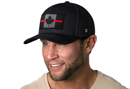black trucker hat worn by a male model viewed from the left side and features a Thin Red Line Tactical Canadian Flag Embroidered Rectangle Patch displayed on the front panel. The hat has a classic mesh back design and a curved structured bill