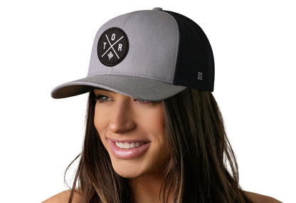 Gray-Black trucker hat worn by a female model viewed from the left side and features a Toronto TOR X Embroidered Circle Patch displayed on the front panel. The hat has a classic mesh back design and a curved structured bill