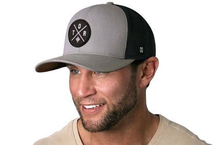 Gray-Black trucker hat worn by a male model viewed from the left side and features a Toronto TOR X Embroidered Circle Patch displayed on the front panel. The hat has a classic mesh back design and a curved structured bill