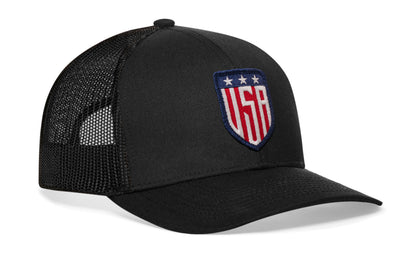 Black trucker hat viewed from the right side, showcasing a USA Puff Embroidered Shield Patch prominently displayed on the front