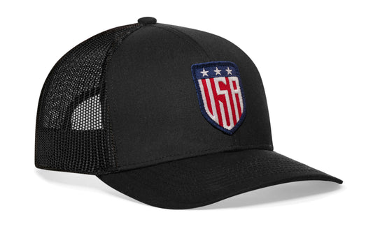 Black trucker hat viewed from the right side, showcasing a USA Puff Embroidered Shield Patch prominently displayed on the front