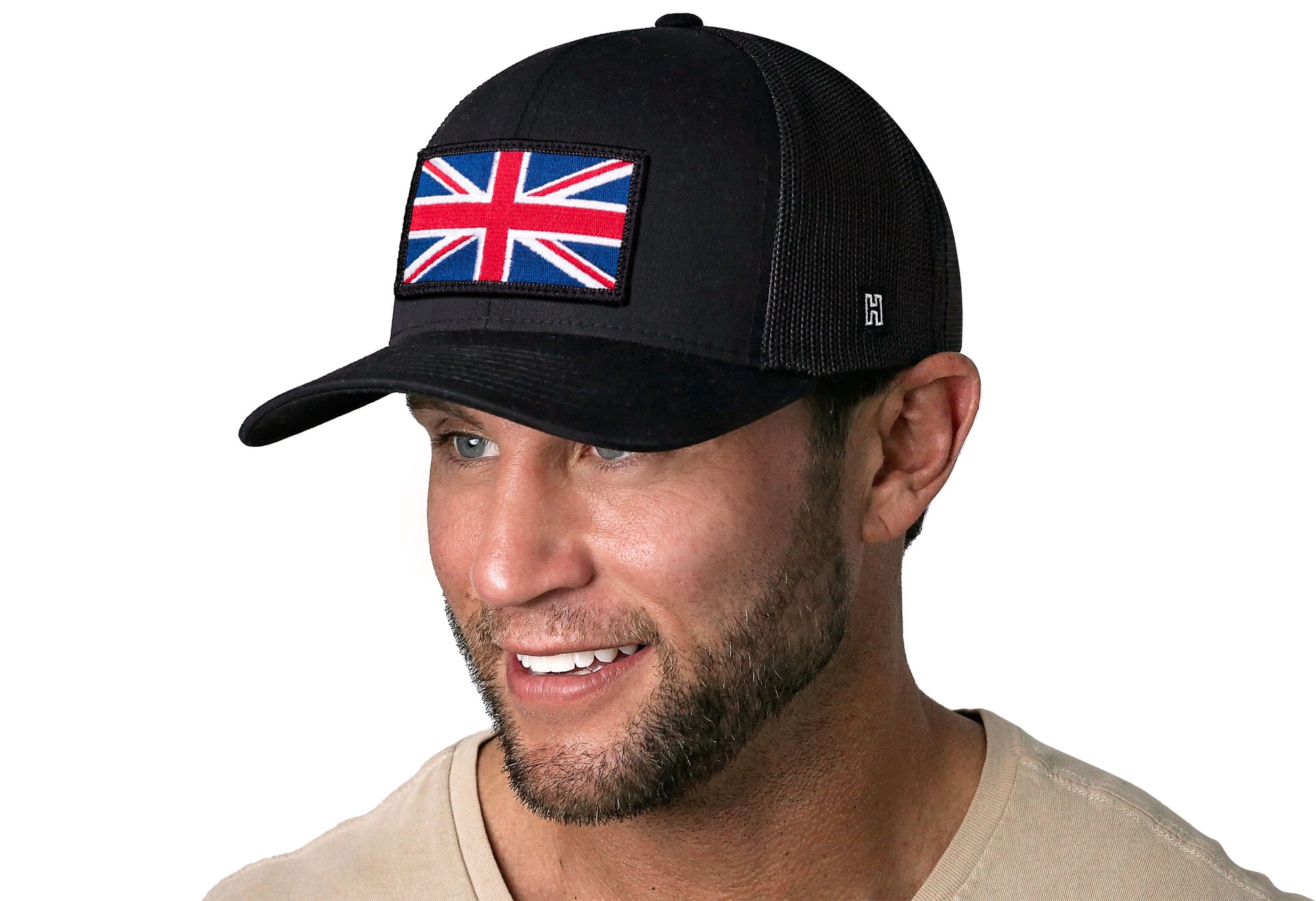 Black trucker hat worn by a male model viewed from the left side and features a United Kingdom Flag Embroidered Rectangle Patch displayed on the front panel. The hat has a classic mesh back design and a curved structured bill