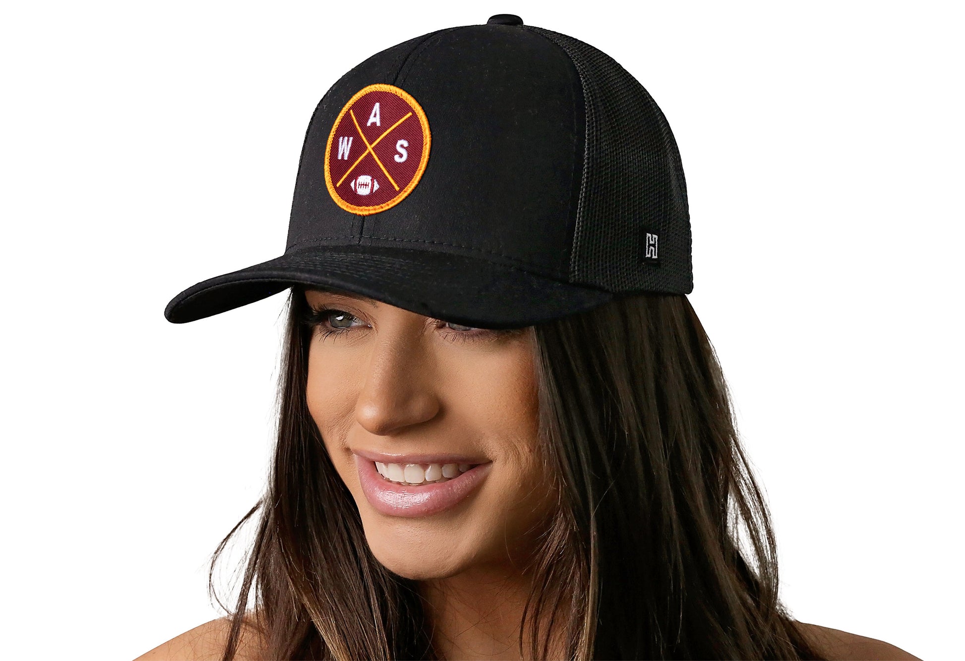 black trucker hat worn by a female model viewed from the left side and features a bold burgundy and gold embroidered X patch displayed on the front panel. The hat has a classic mesh back design and a curved structured bill