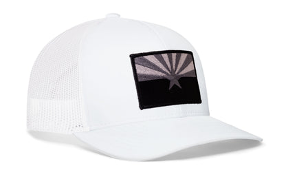white trucker hat viewed from the right side, showcasing a bold black and gray embroidered flag patch prominently displayed on the front