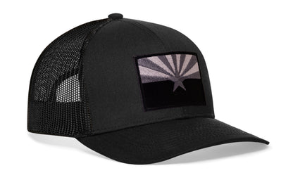 black trucker hat viewed from the right side, showcasing a bold black and gray embroidered flag patch prominently displayed on the front