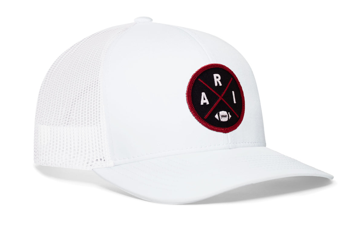 white trucker hat viewed from the right side, showcasing a bold red and black embroidered X patch prominently displayed on the front