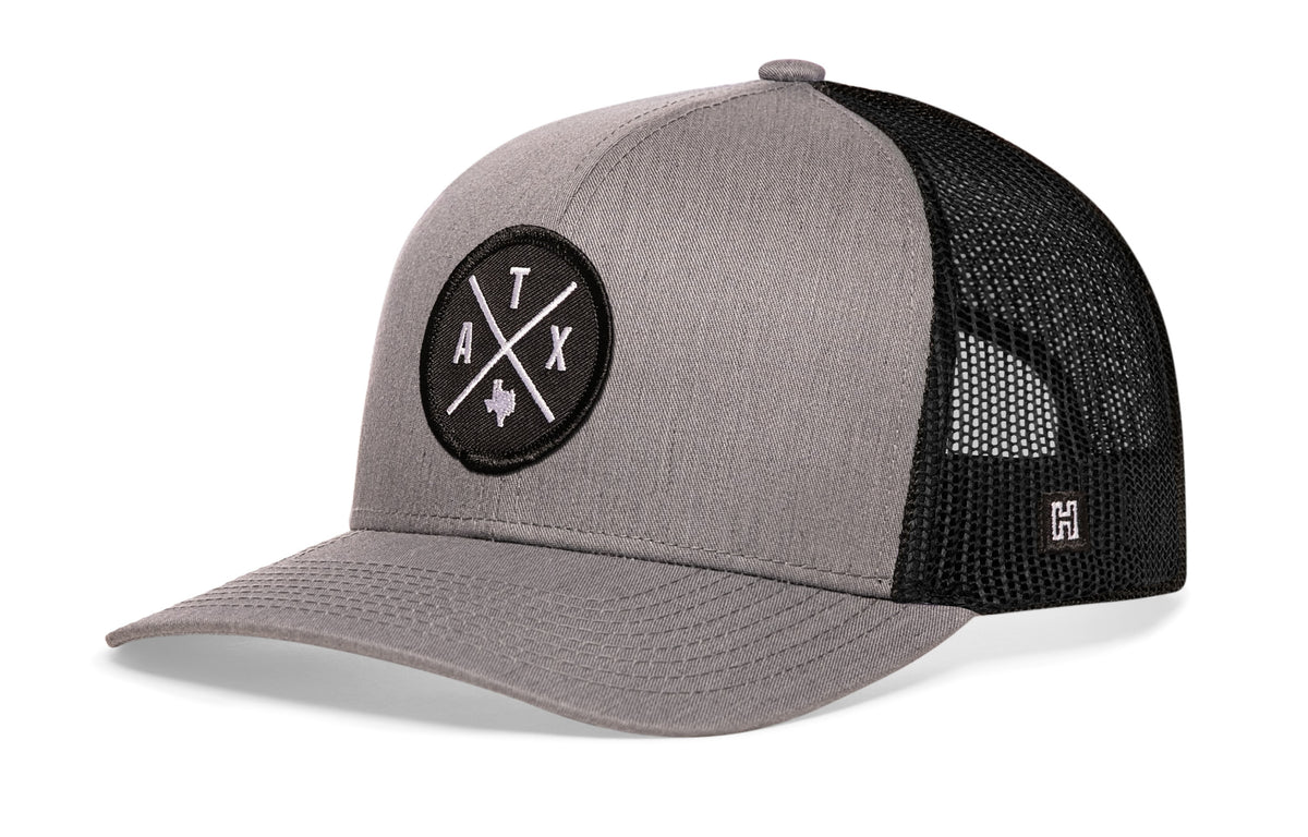 Austin Trucker Hat, gray-black snapback showing Haka brandmark on left side of cap.