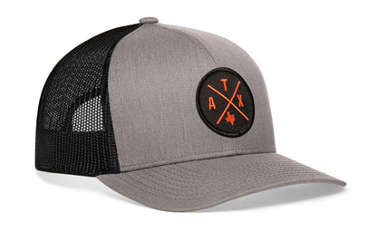 gray-black trucker hat viewed from the right side, showcasing a bold orange embroidered X patch prominently displayed on the front