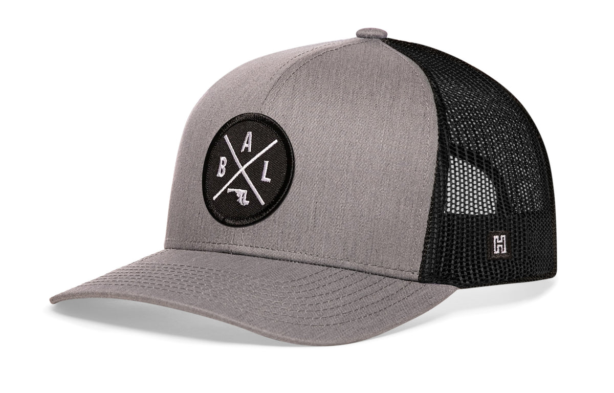 Baltimore Trucker Hat, gray-black snapback showing Haka brandmark on left side of cap.