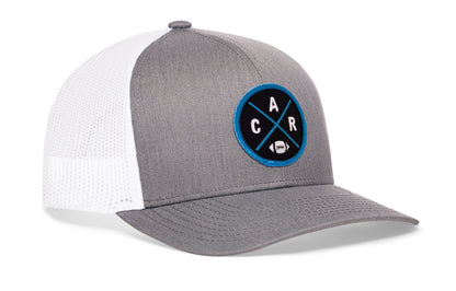 gray-white trucker hat viewed from the right side, showcasing a bold blue and black embroidered X patch prominently displayed on the front