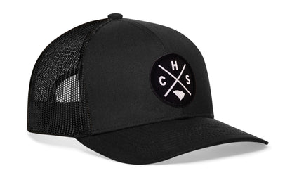 black trucker hat viewed from the right side, showcasing a bold black and white embroidered X patch prominently displayed on the front
