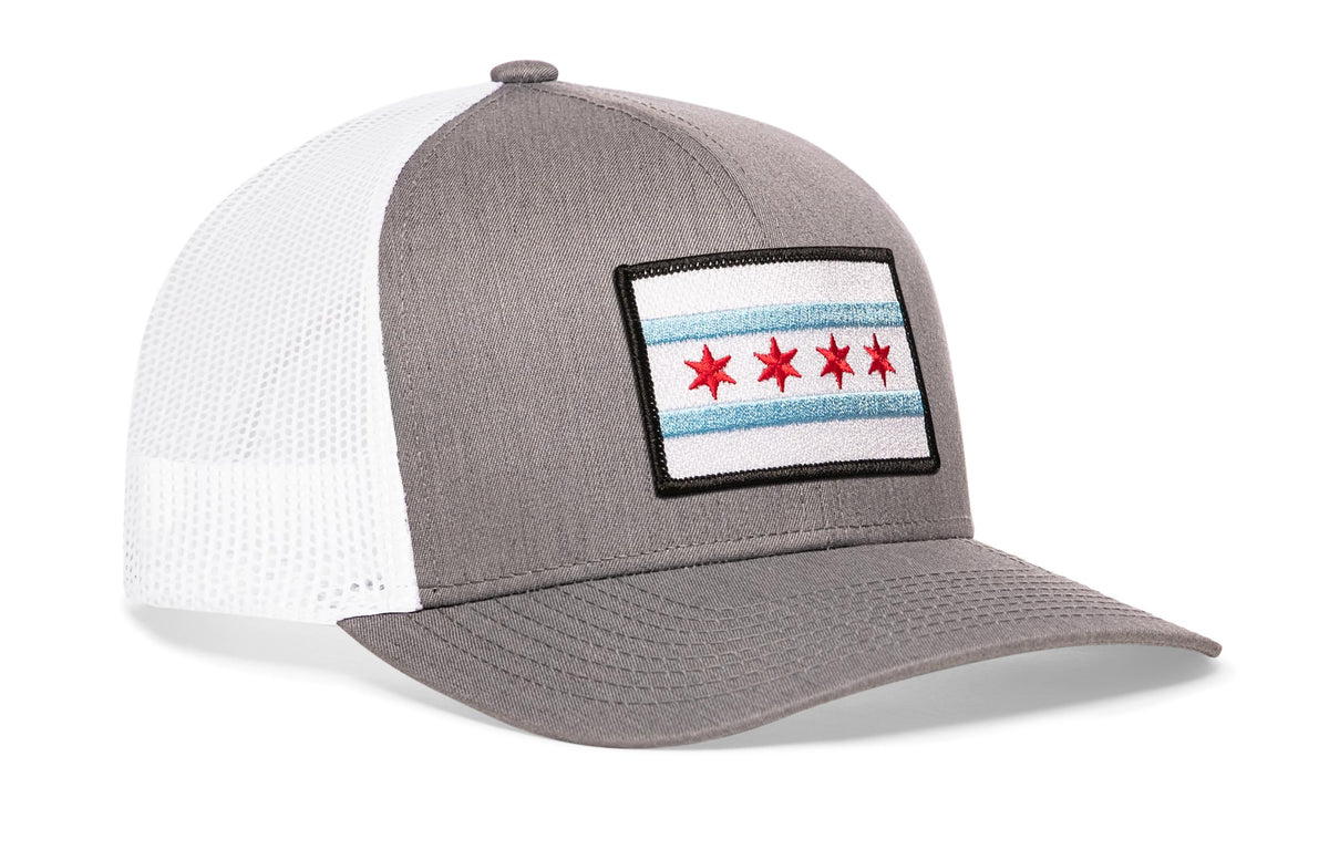 gray-white trucker hat viewed from the right side, showcasing a bold red and light blue embroidered flag patch prominently displayed on the front