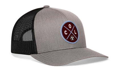 gray-black trucker hat viewed from the right side, showcasing a bold burgundy and blue embroidered X patch prominently displayed on the front