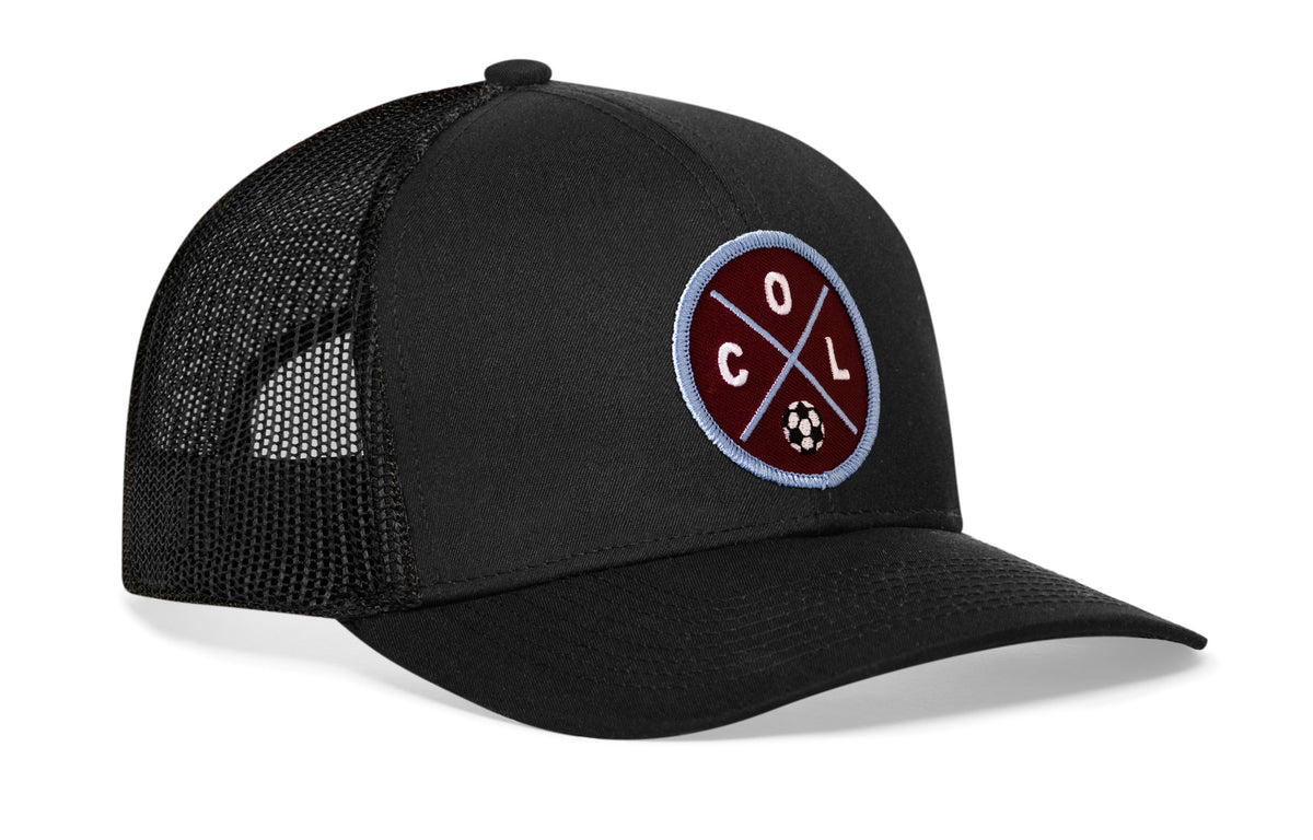 black trucker hat viewed from the right side, showcasing a bold burgundy and blue embroidered X patch prominently displayed on the front