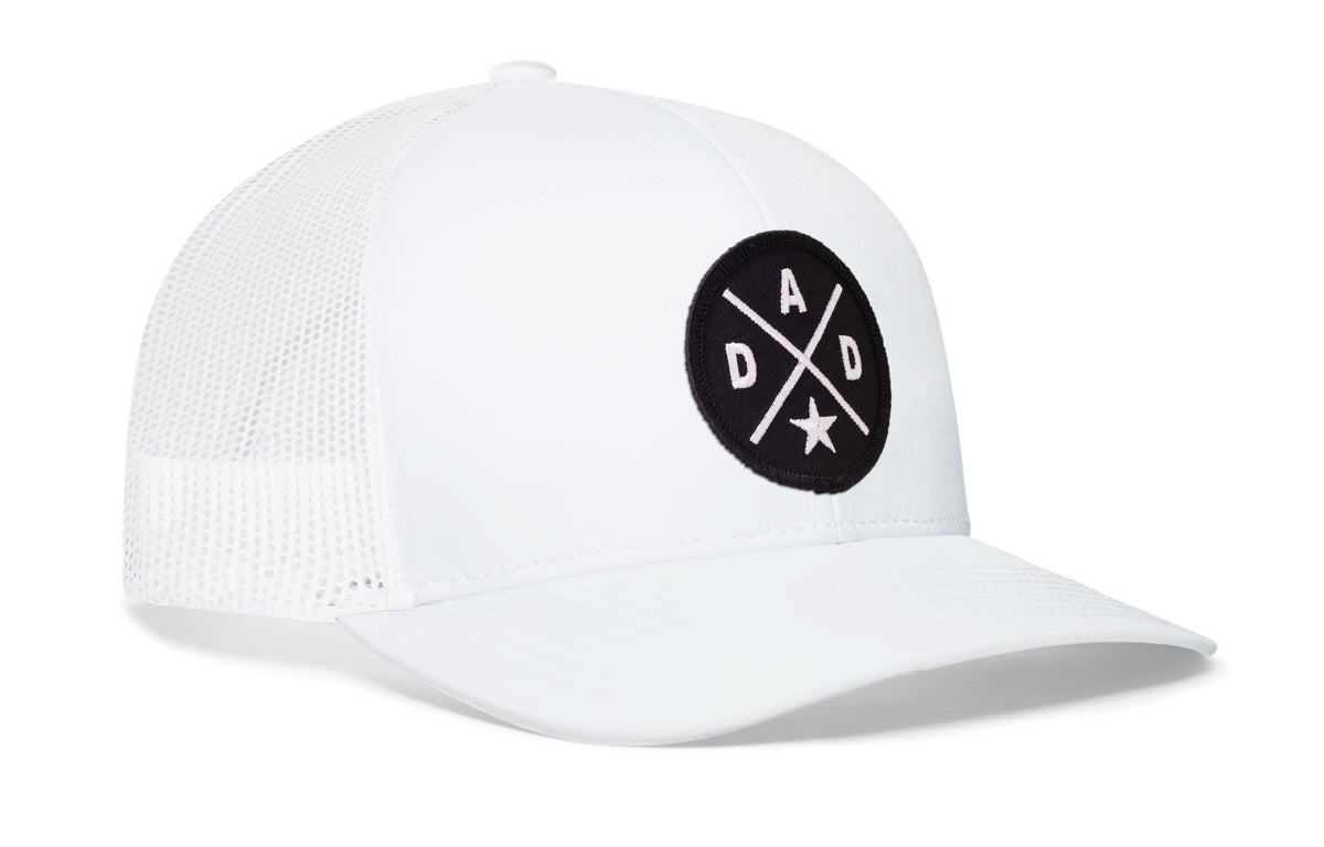 white trucker hat viewed from the right side, showcasing a bold black and white embroidered X patch prominently displayed on the front