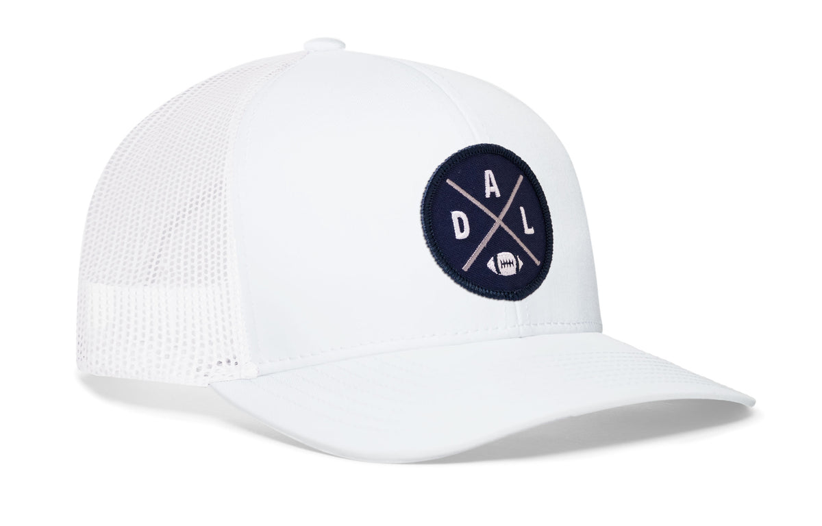 white trucker hat viewed from the right side, showcasing a bold navy blue and silver embroidered X patch prominently displayed on the front
