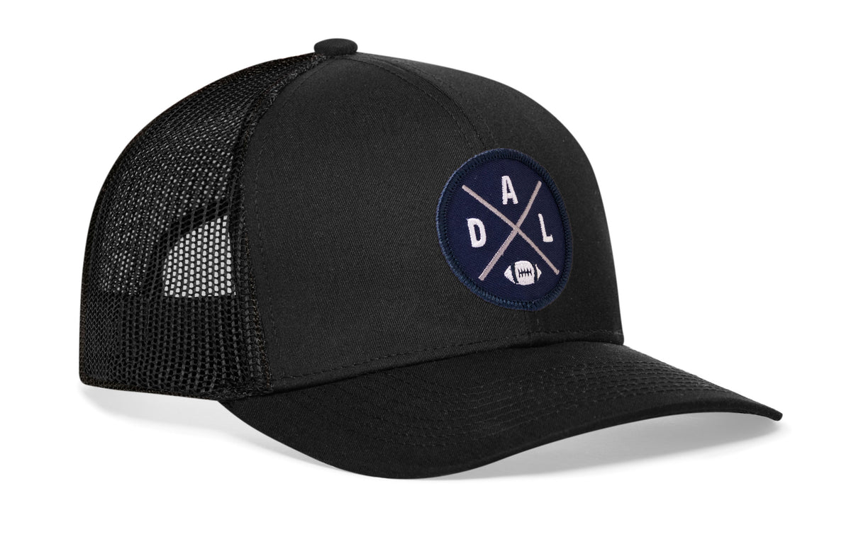 black trucker hat viewed from the right side, showcasing a bold navy blue and silver embroidered X patch prominently displayed on the front