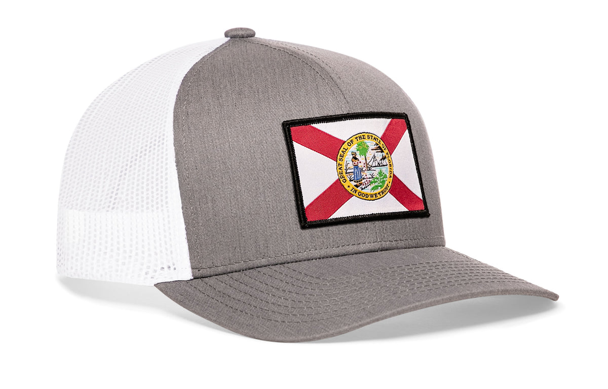 gray-white trucker hat viewed from the right side, showcasing a bold red, white and yellow woven patch prominently displayed on the front