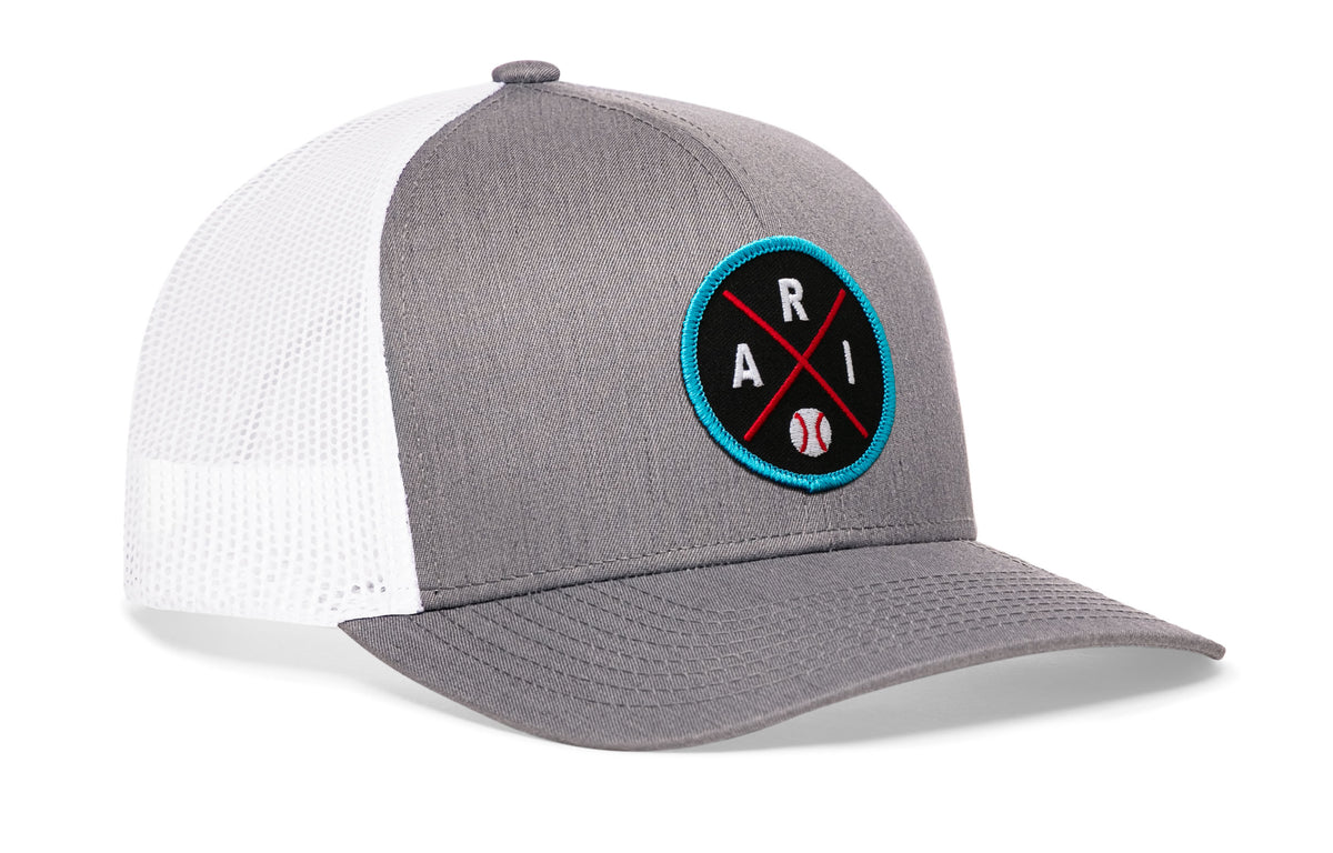 gray-white trucker hat viewed from the right side, showcasing a bold black, red and columbia blue embroidered X patch prominently displayed on the front