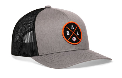 gray-black trucker hat viewed from the right side, showcasing a bold black and orange embroidered X patch prominently displayed on the front