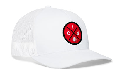 white trucker hat viewed from the right side, showcasing a red and black baseball embroidered X patch prominently displayed on the front