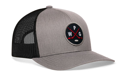 gray-black trucker hat viewed from the right side, showcasing a bold navy, red and gray embroidered X patch prominently displayed on the front