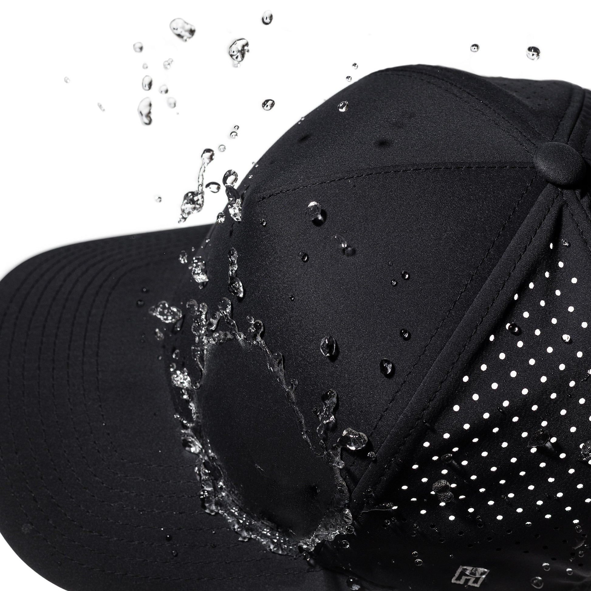 Black performance hat with water droplets splashing onto it against a white background