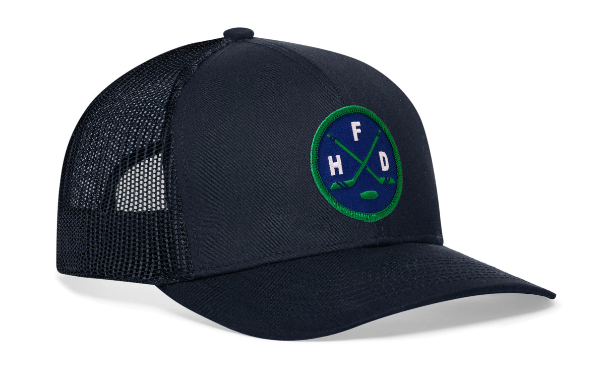 navy trucker hat viewed from the right side, showcasing a bold navy and green embroidered X patch prominently displayed on the front