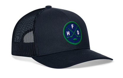 navy trucker hat viewed from the right side, showcasing a bold navy and green embroidered X patch prominently displayed on the front